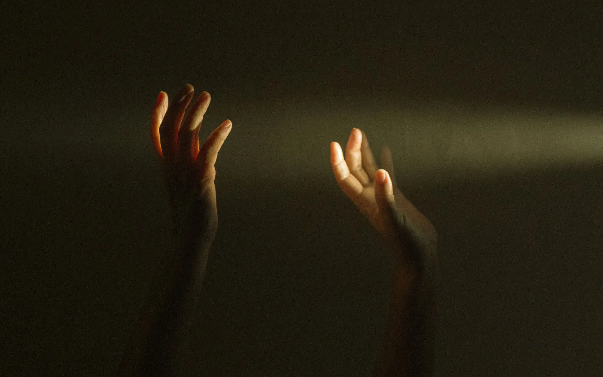 Two hands in the dark reaching out and dancing in a beam of light